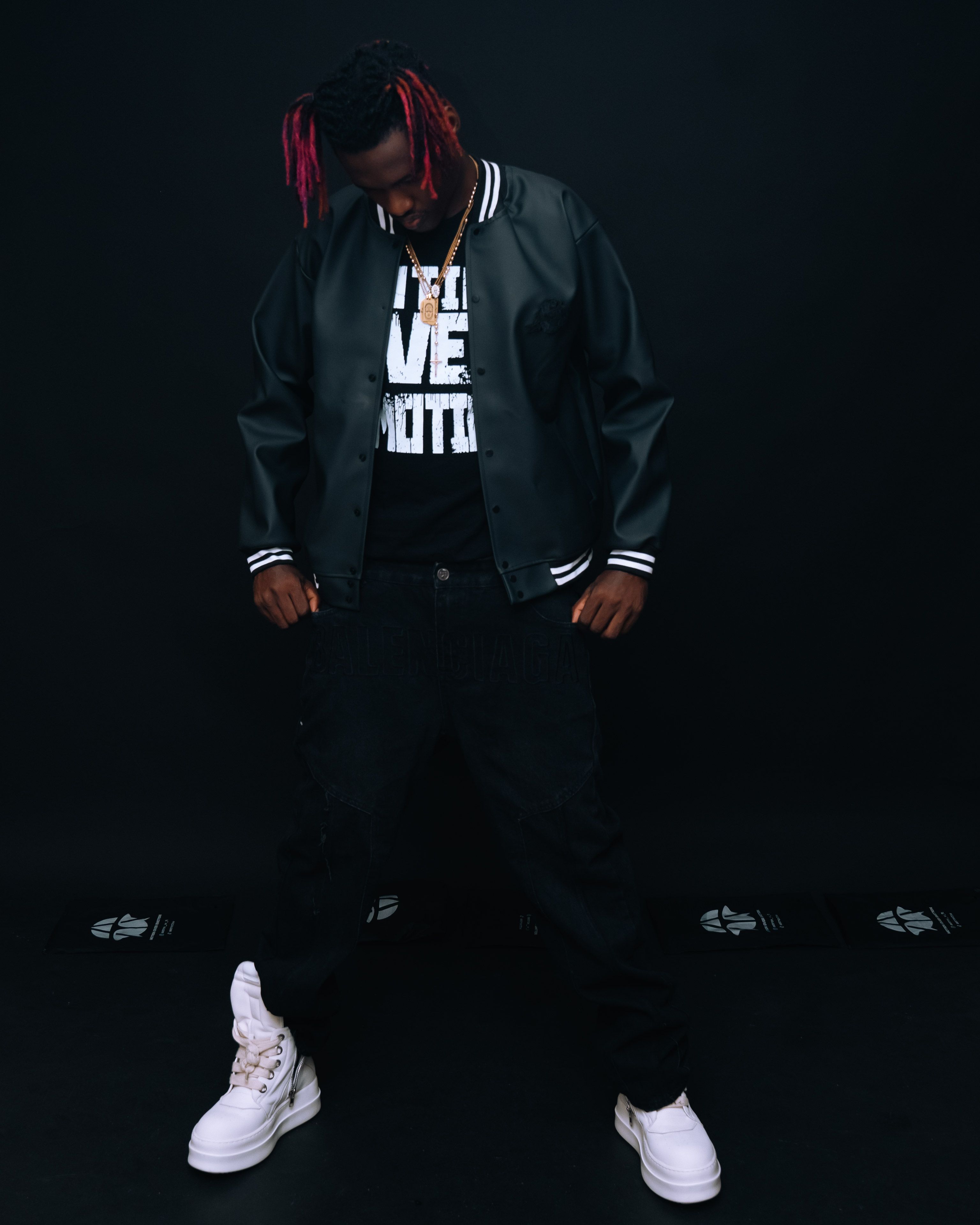 Person in trendy streetwear jacket and sneakers posing against dark background.