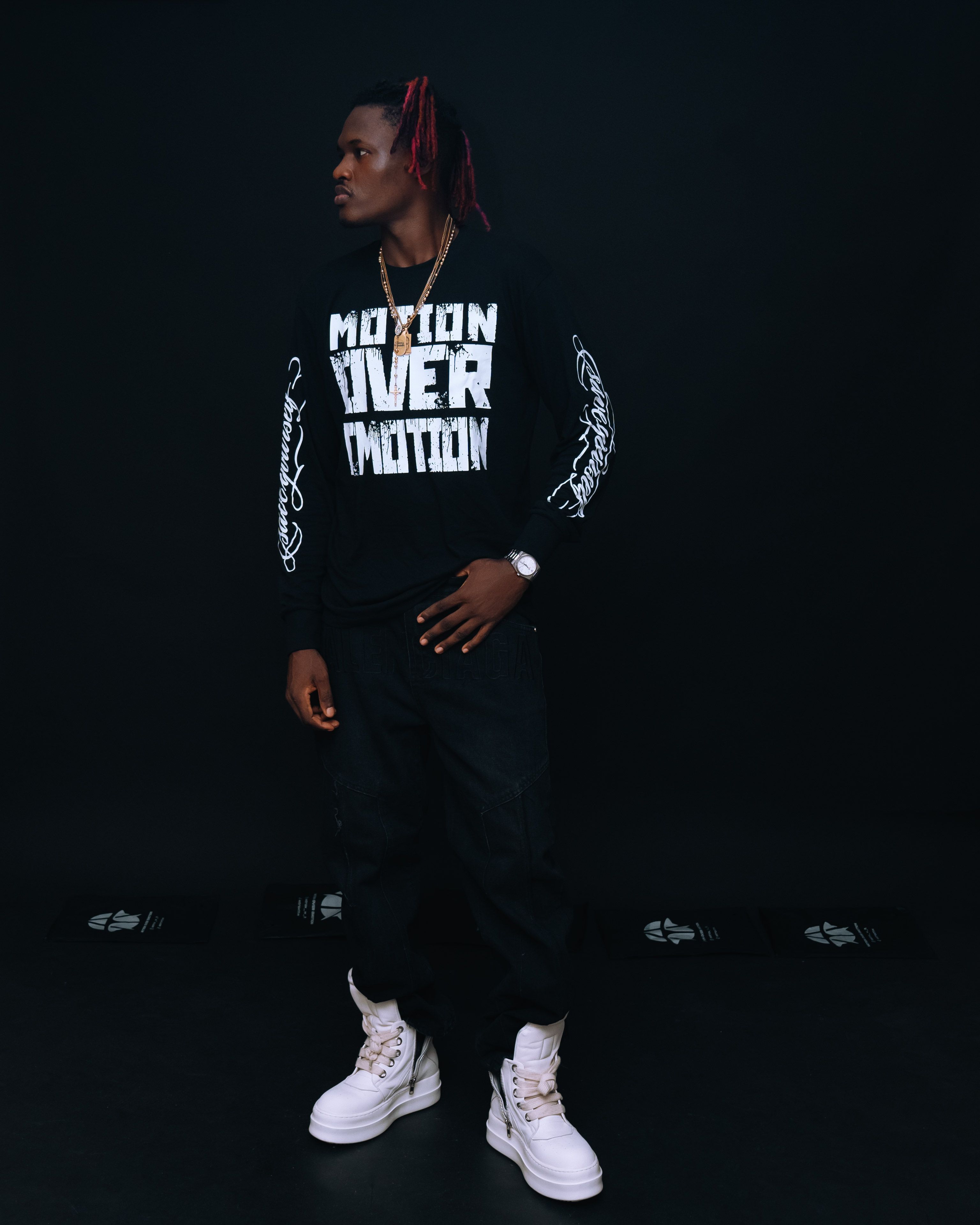 Young man in trendy streetwear poses confidently in dark studio setting.