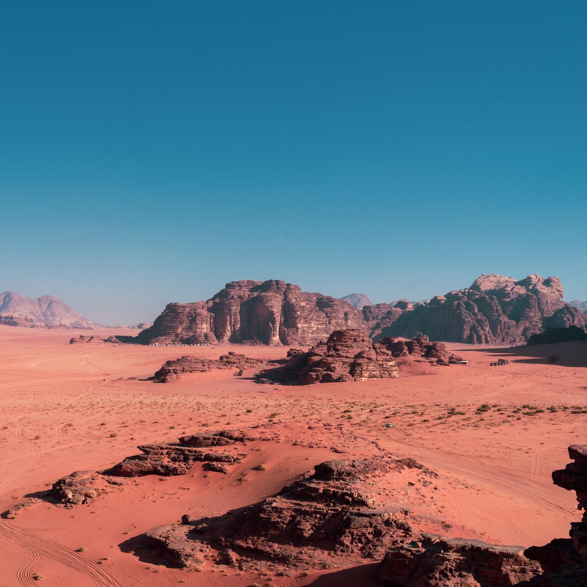 Red desert floor and sandstone mountains of Wadi Rum under blue sky