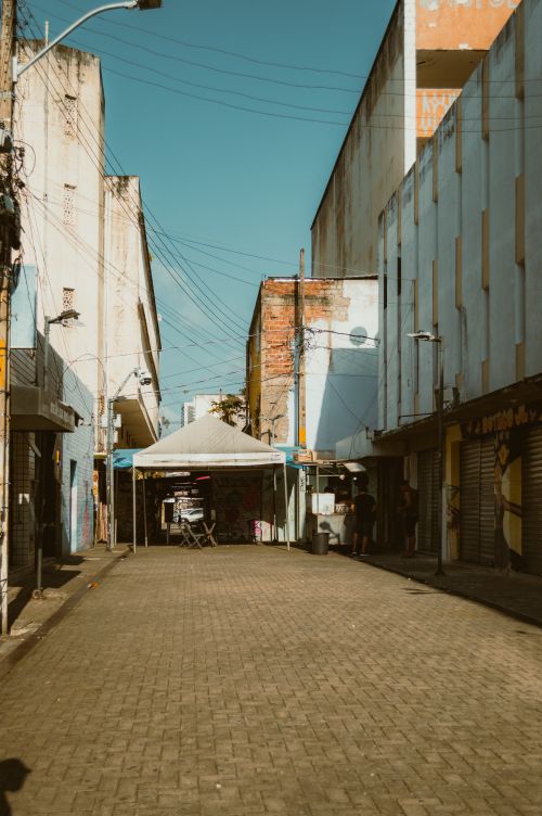 Free An empty street in RN, Brazil, with closed shops and a clear blue sky, creating a vintage urban atmosphere. Stock Photo