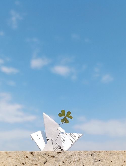 Free Origami bird with a clover leaf against a clear blue sky, symbolizing luck and simplicity. Stock Photo