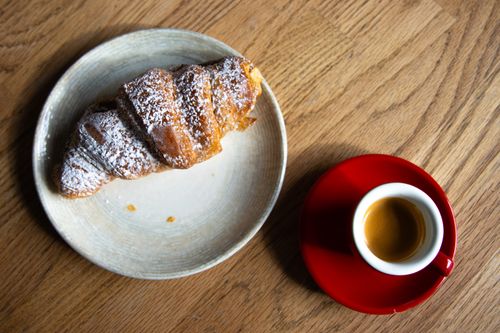 Free A flaky croissant on a plate with a cup of espresso on a wooden table. Stock Photo