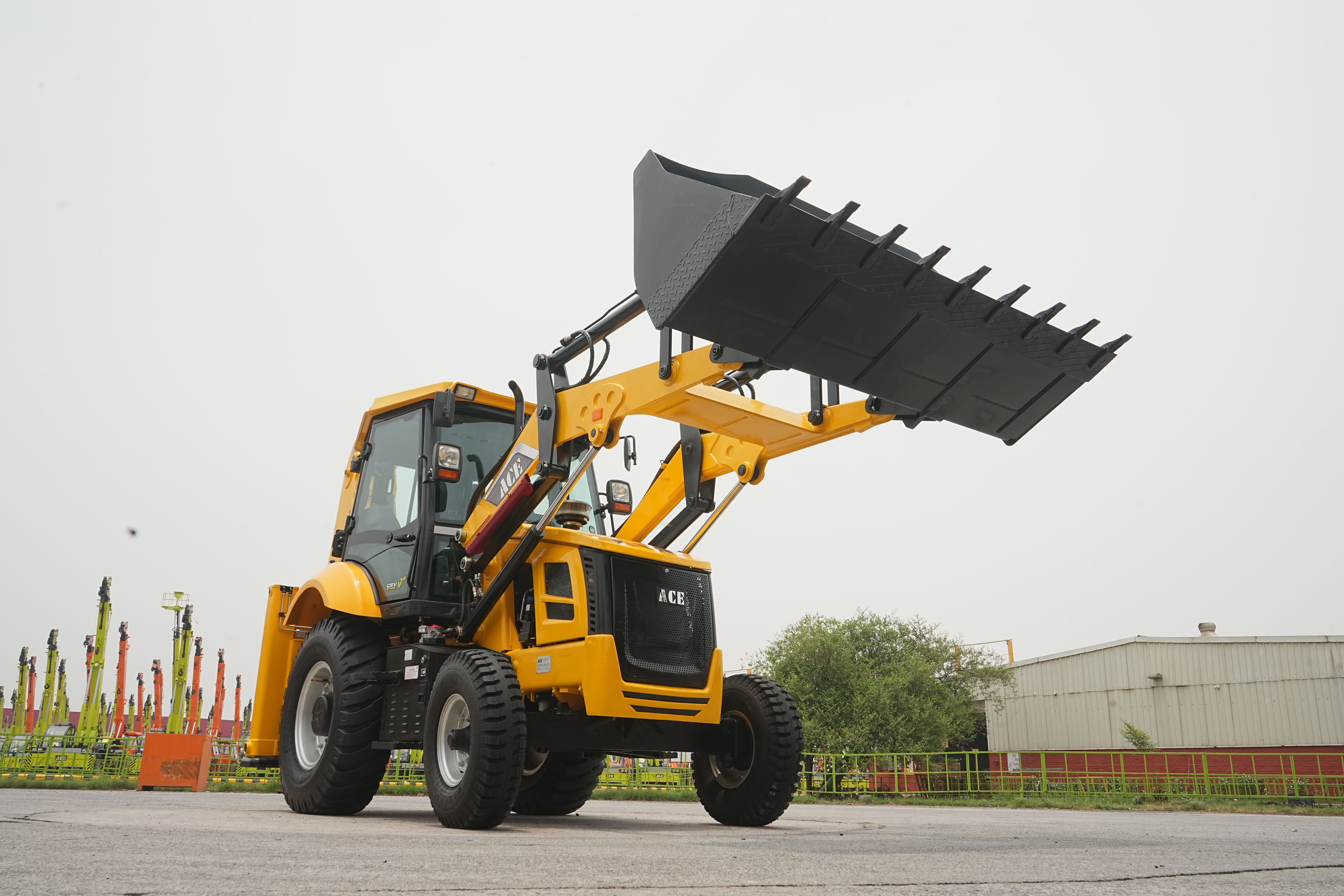 ACE backhoe loader with raised shovel against industrial background in Faridabad.