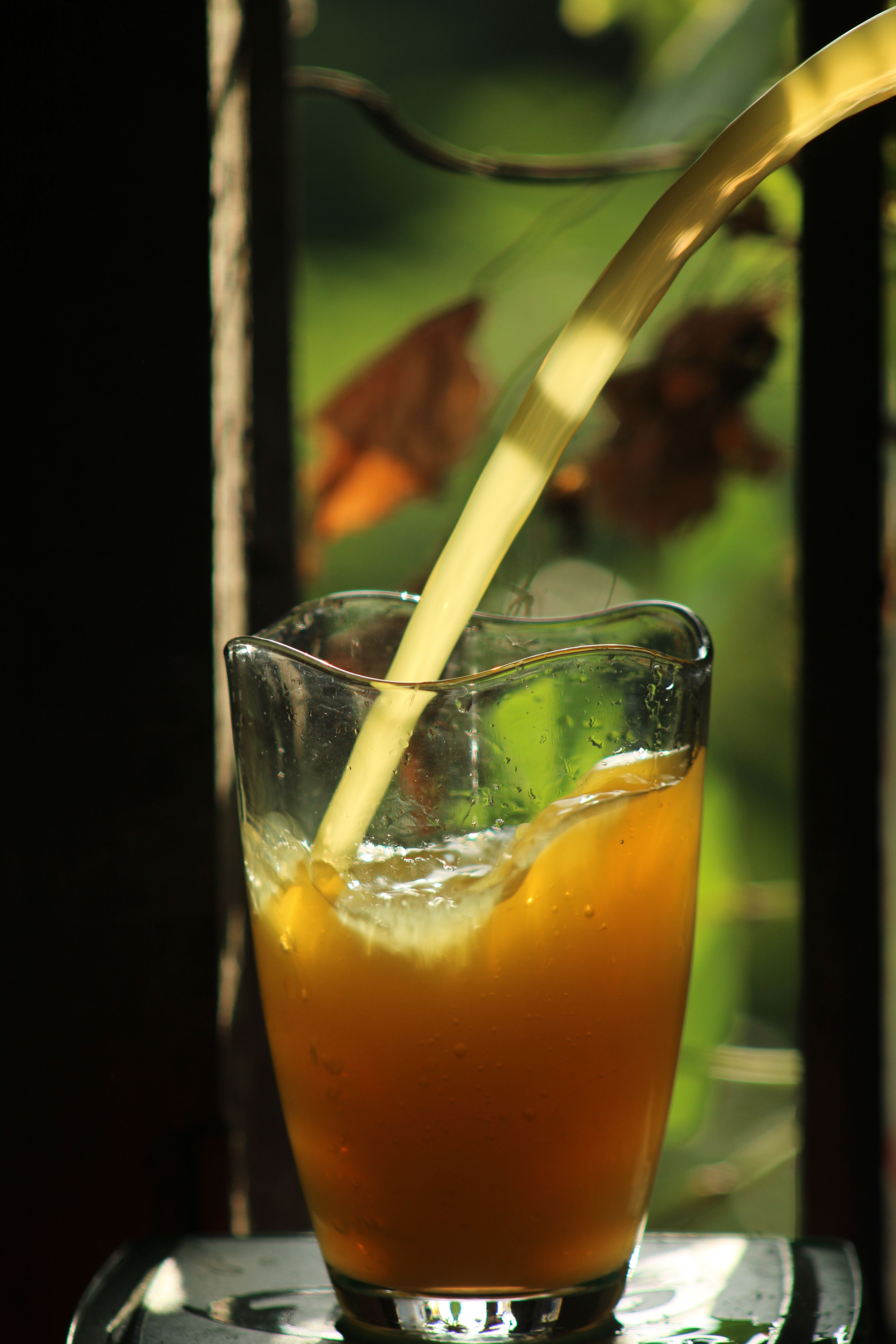 Jus d'orange versé dans un verre, lumière du matin à contre-jour, verdure floue en arrière-plan