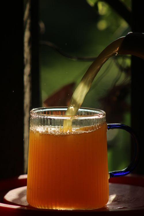 Free Sunlit orange juice being poured into glass with blue handle, perfect for healthy lifestyle theme. Stock Photo