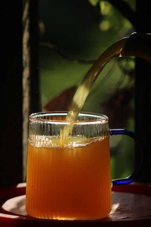 Free Close-up of orange juice being poured into a glass mug with sunlight highlighting it. Stock Photo