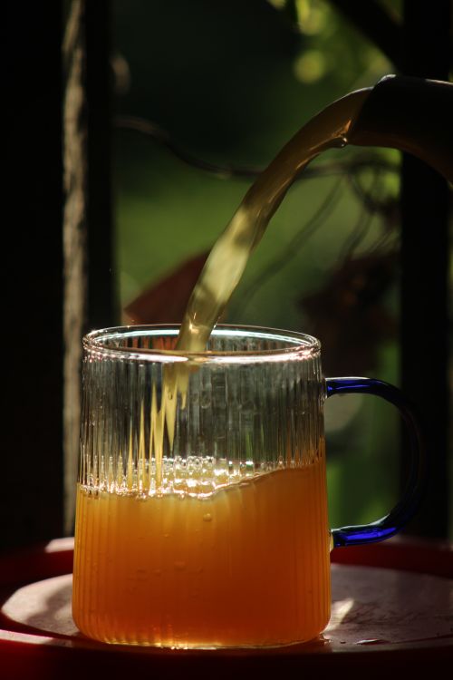 Free Close-up of apple juice being poured into a ribbed glass mug with sunlight highlighting the beverage. Stock Photo