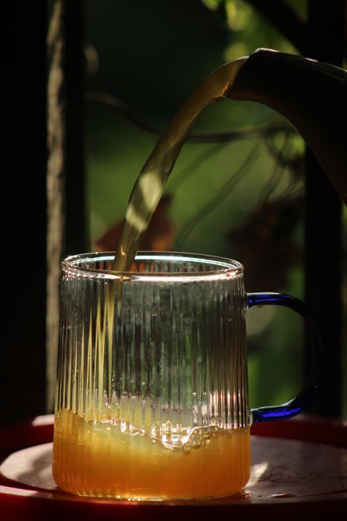 Free Close-up of orange juice being poured into a ribbed glass mug with sunlight illuminating the scene. Stock Photo