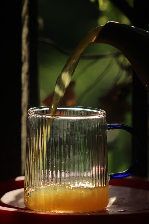 Free Sunlight casts shadows as juice is poured into a textured glass mug outdoors. Stock Photo