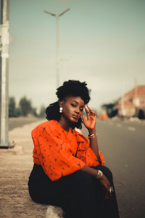 Free Confident woman in vibrant red top sitting on a street edge, exuding urban style. Stock Photo
