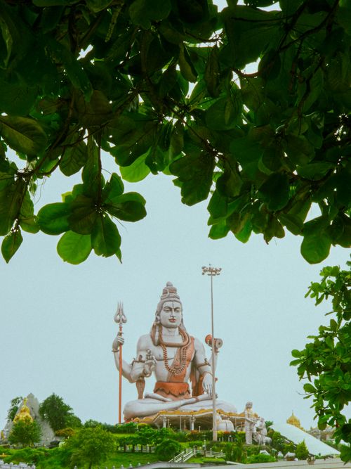 Free Majestic statue of Lord Shiva seen through rich foliage, offering a serene spiritual ambiance. Stock Photo