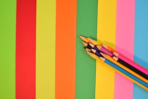 Free Top view of a rainbow of colored pencils on brightly colored paper sheets. Stock Photo