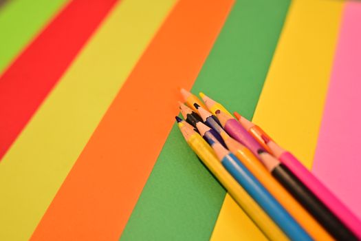 Bright colored pencils on a vibrant, striped paper background, showcasing creativity and art.