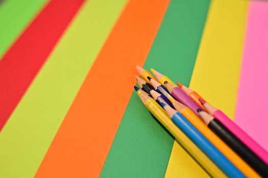 A collection of colored pencils rests on vivid sheets of paper, showcasing a burst of creative color.