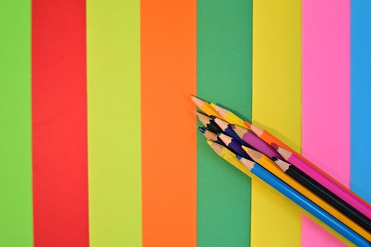 A vibrant display of colored pencils placed on a colorful striped paper background.