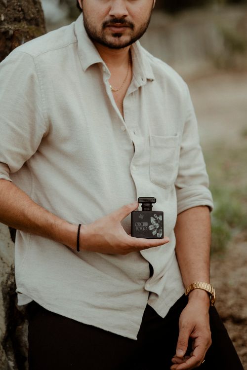 Free A fashionable man holds a perfume bottle outdoors, embodying modern style and elegance. Stock Photo