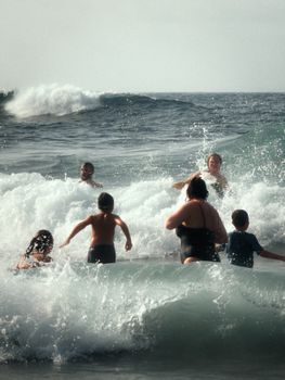 People swimming in big waves at a Tenerife beach, enjoying the summer sun.
