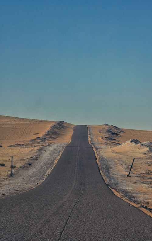 Free A long, straight desert highway stretching into the horizon under a clear blue sky. Stock Photo