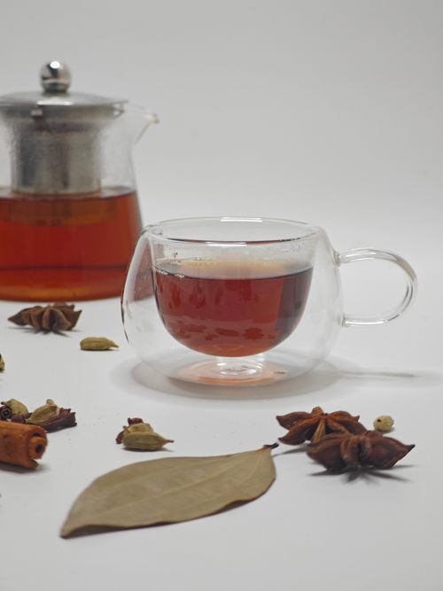 Free A clear glass tea set with spices like cinnamon, star anise, and cardamom on a white surface. Stock Photo