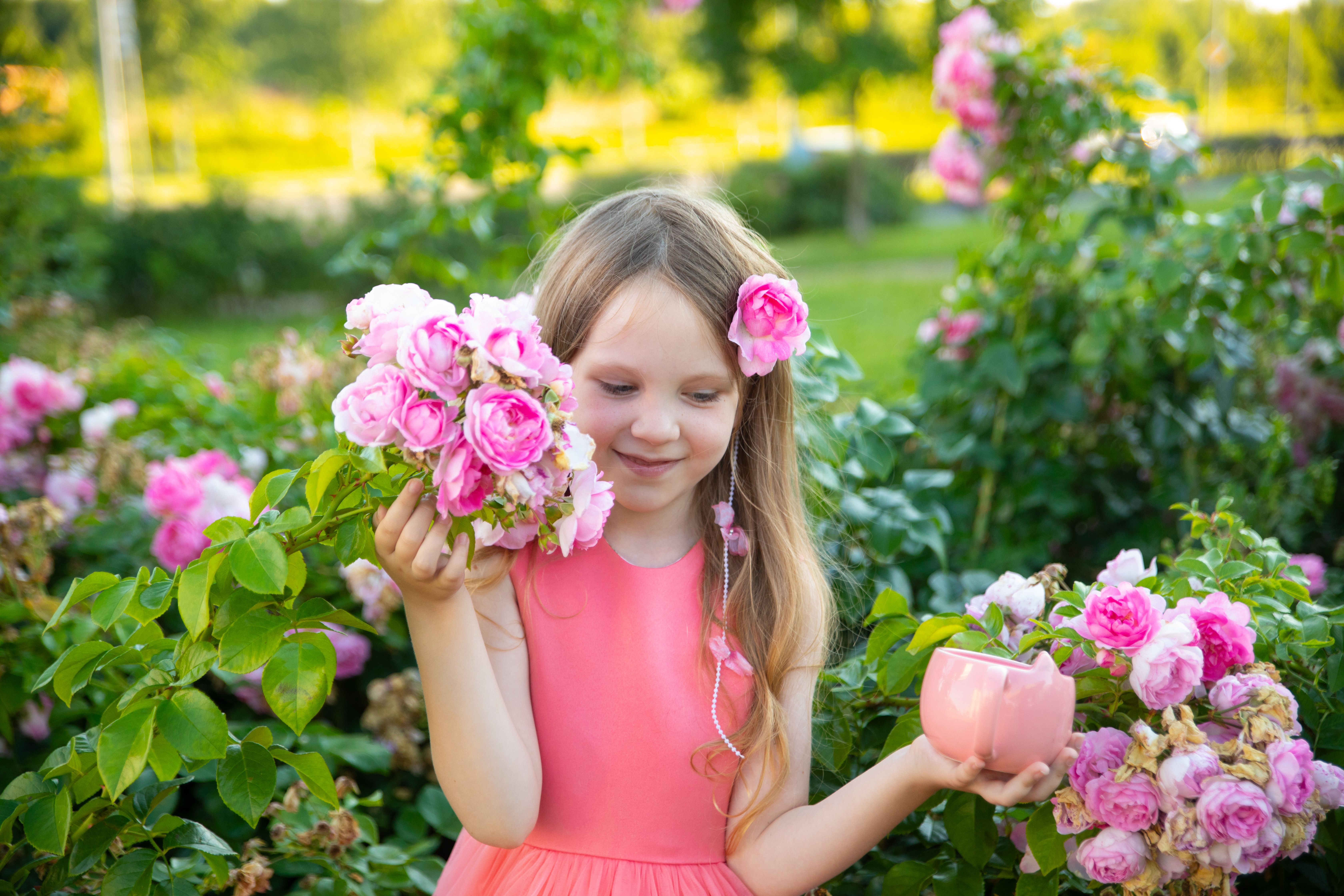 A young girl in a pink dress enjoying a vibrant rose garden, capturing a joyful summer moment.