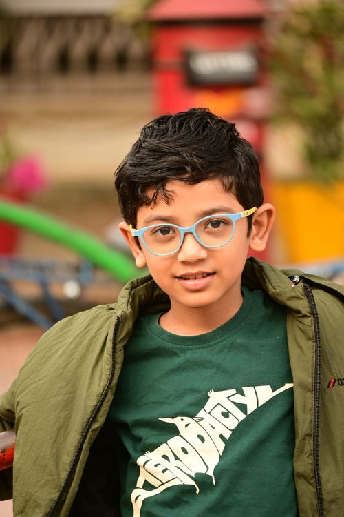 Free Portrait of a child wearing glasses and a green jacket, set against a vibrant outdoor background. Stock Photo