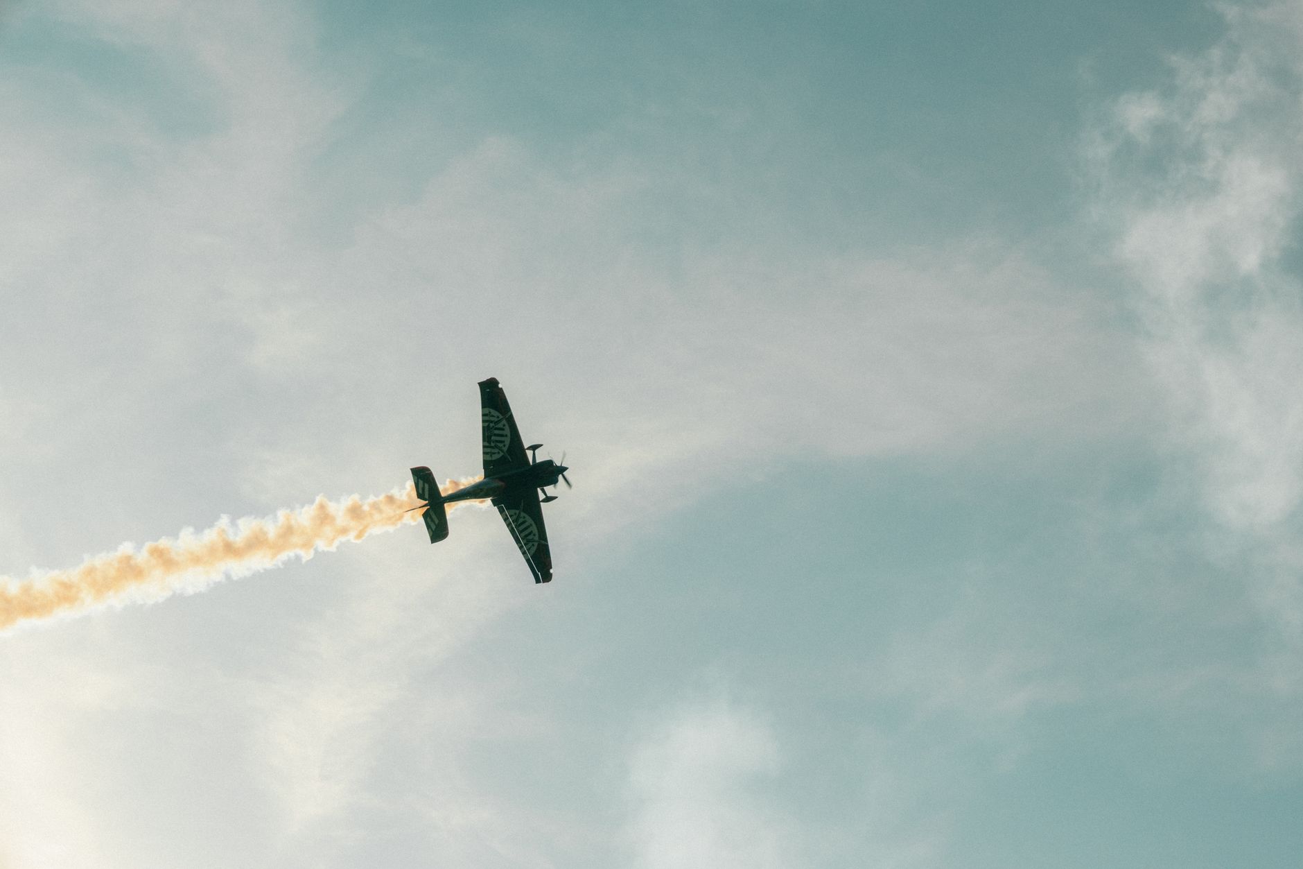 Un avion de voltige effectuant des figures acrobatiques, laissant une traînée de fumée sur un ciel bleu.