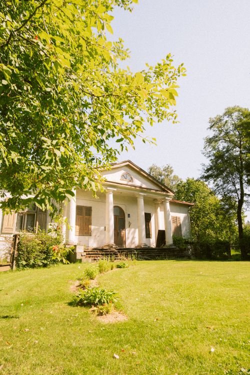 Free A picturesque historic white house surrounded by a lush green garden on a sunny day. Stock Photo