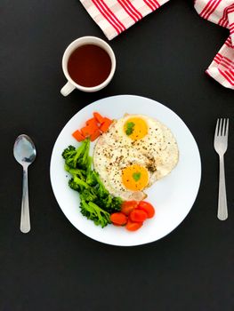 A nutritious breakfast featuring fried eggs, veggies, and tea on a clean black background.