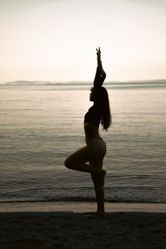 A woman in a yoga pose at the beach during twilight, capturing tranquility and balance.