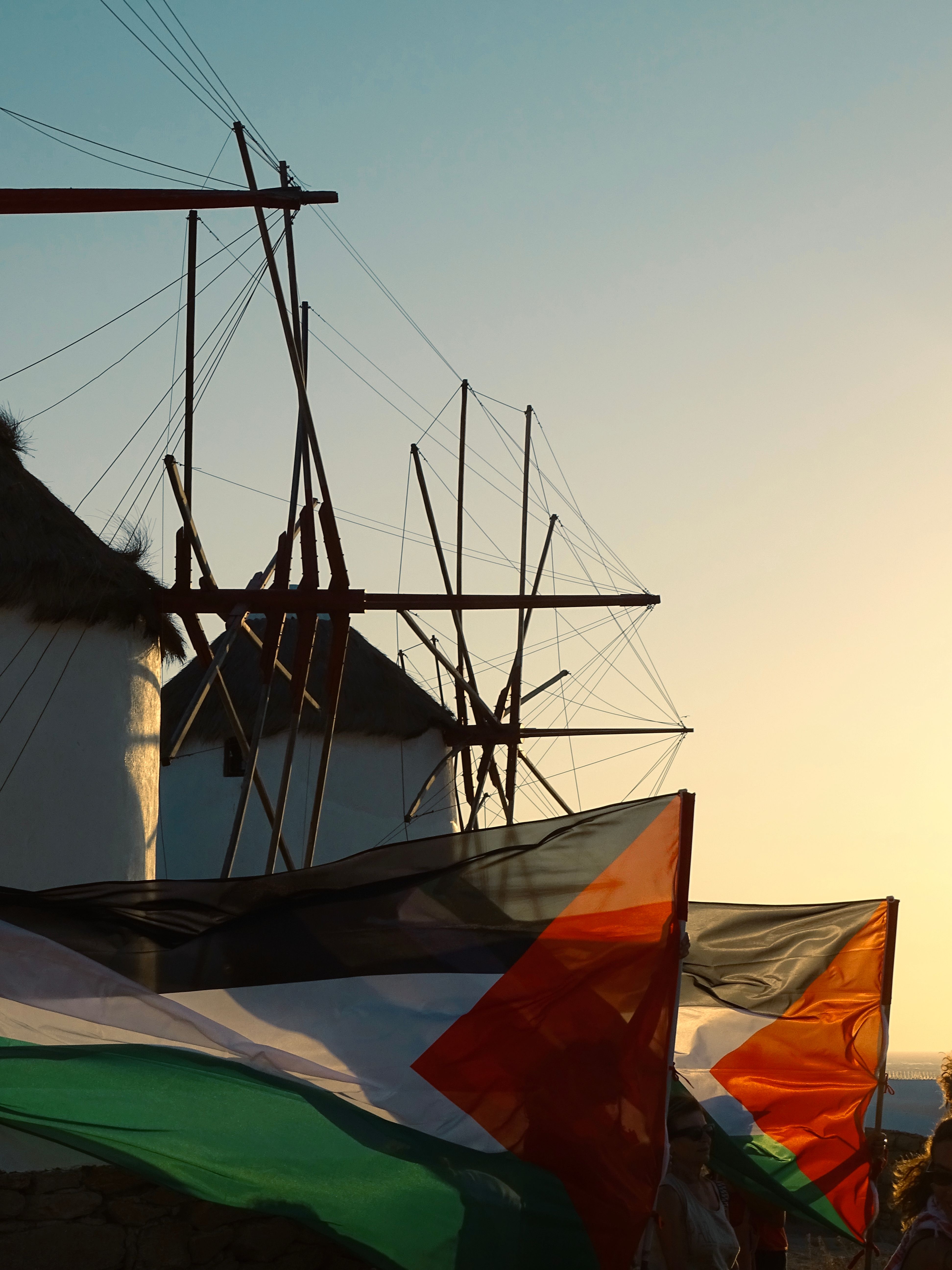 Silhouetted windmills in Mykonos with flags waving in the sunset.