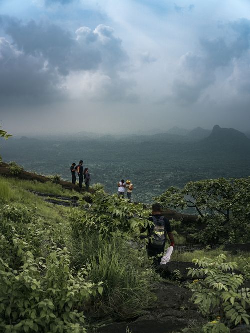 Free Group of hikers enjoying a lush mountain view under a dramatic cloudy sky. Stock Photo