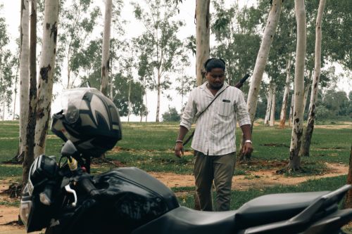 Free A man walks beside a motorcycle in a serene eucalyptus forest, offering a calm outdoor scene. Stock Photo