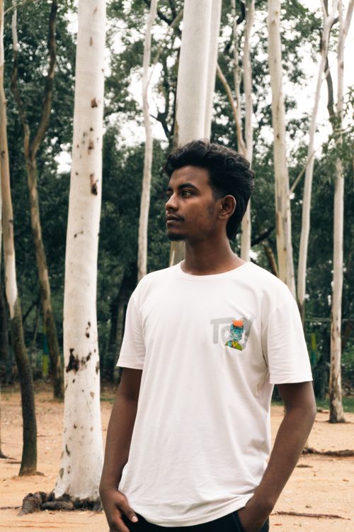 Free A young man stands contemplatively in a lush forest, surrounded by tall trees. Stock Photo