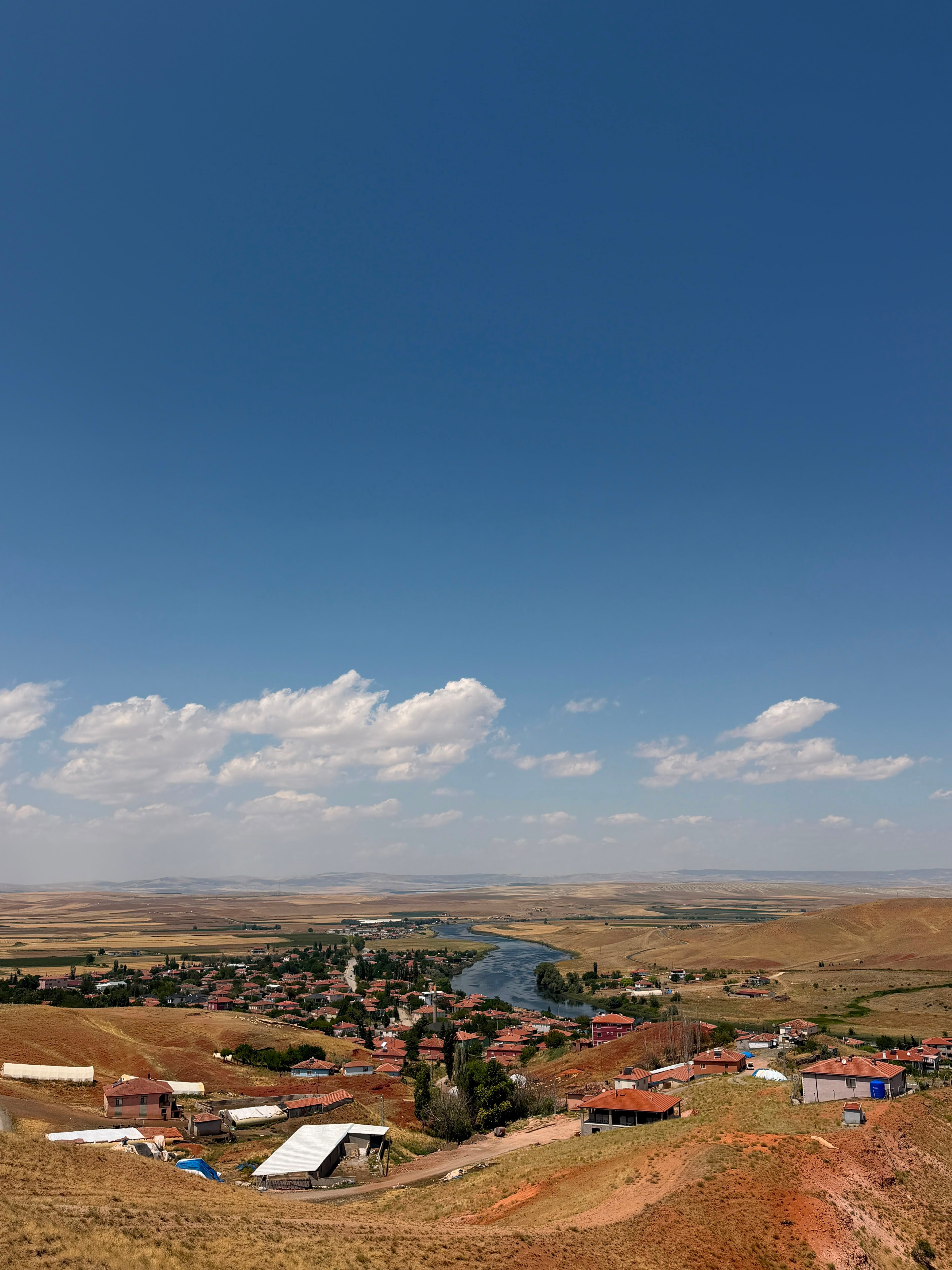 Scenic view of a rural village nestled beside a serene river under a blue sky.