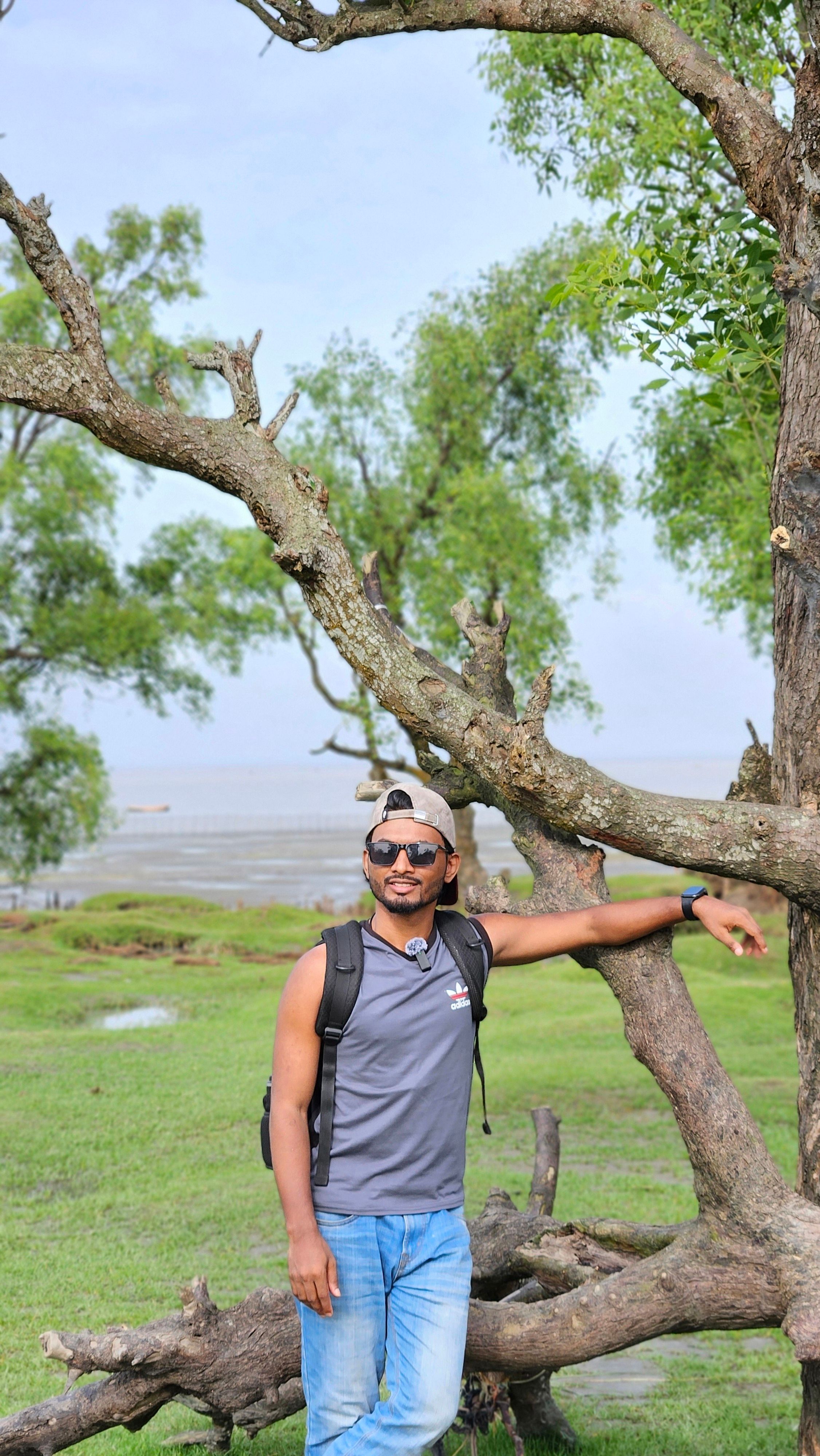 A man enjoys a relaxing day outdoors leaning on a tree, under clear blue skies.