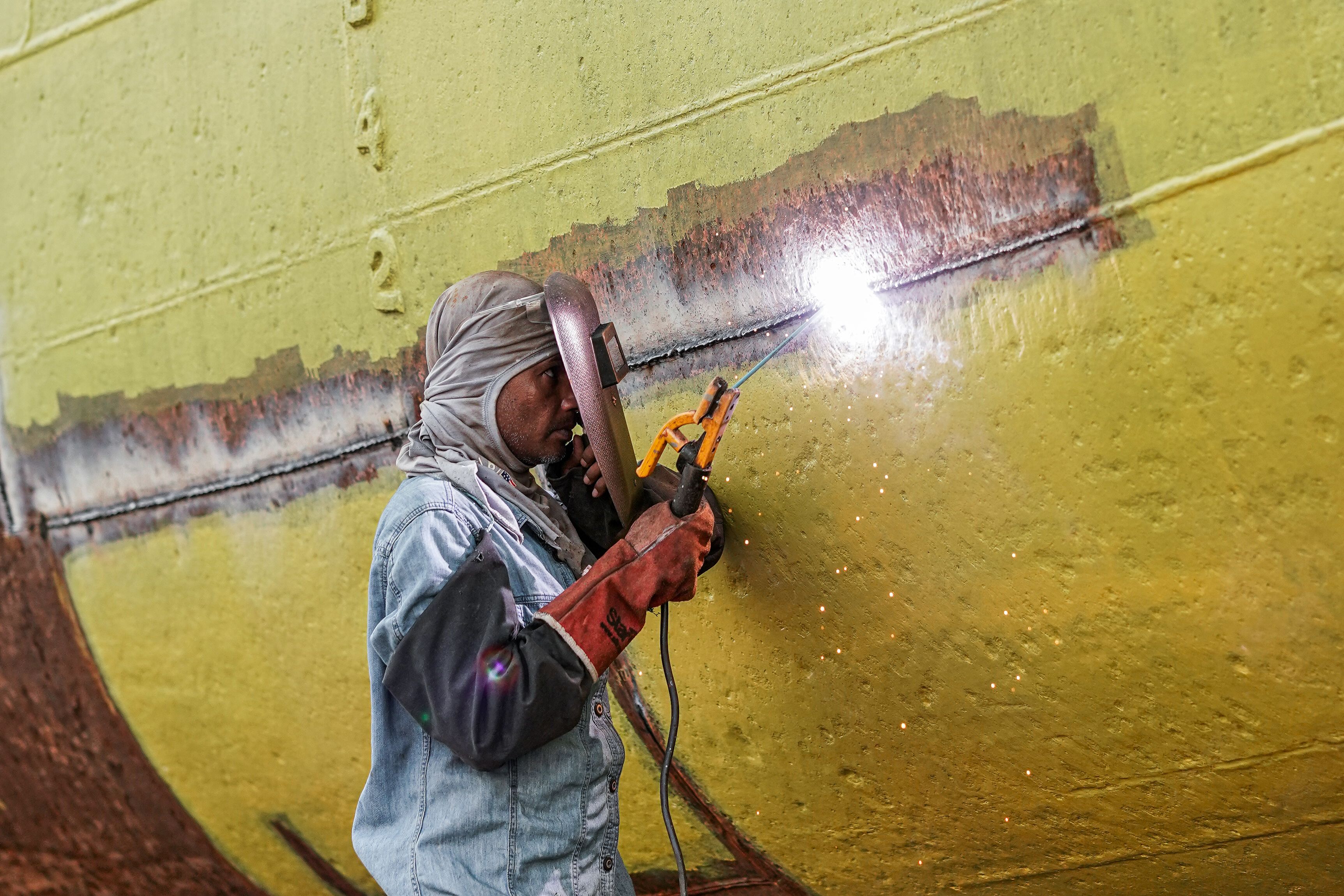 A skilled welder in protective gear works on repairing a large ship's hull.