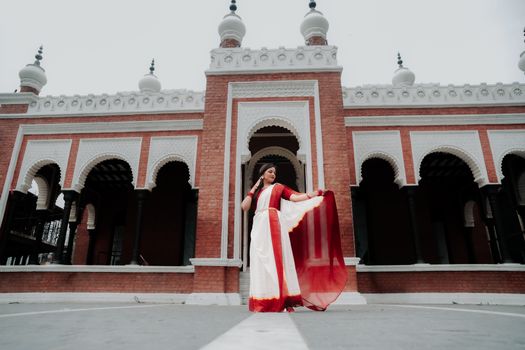 A woman in traditional Indian dress stands gracefully in front of a historic building with ornate architecture.
