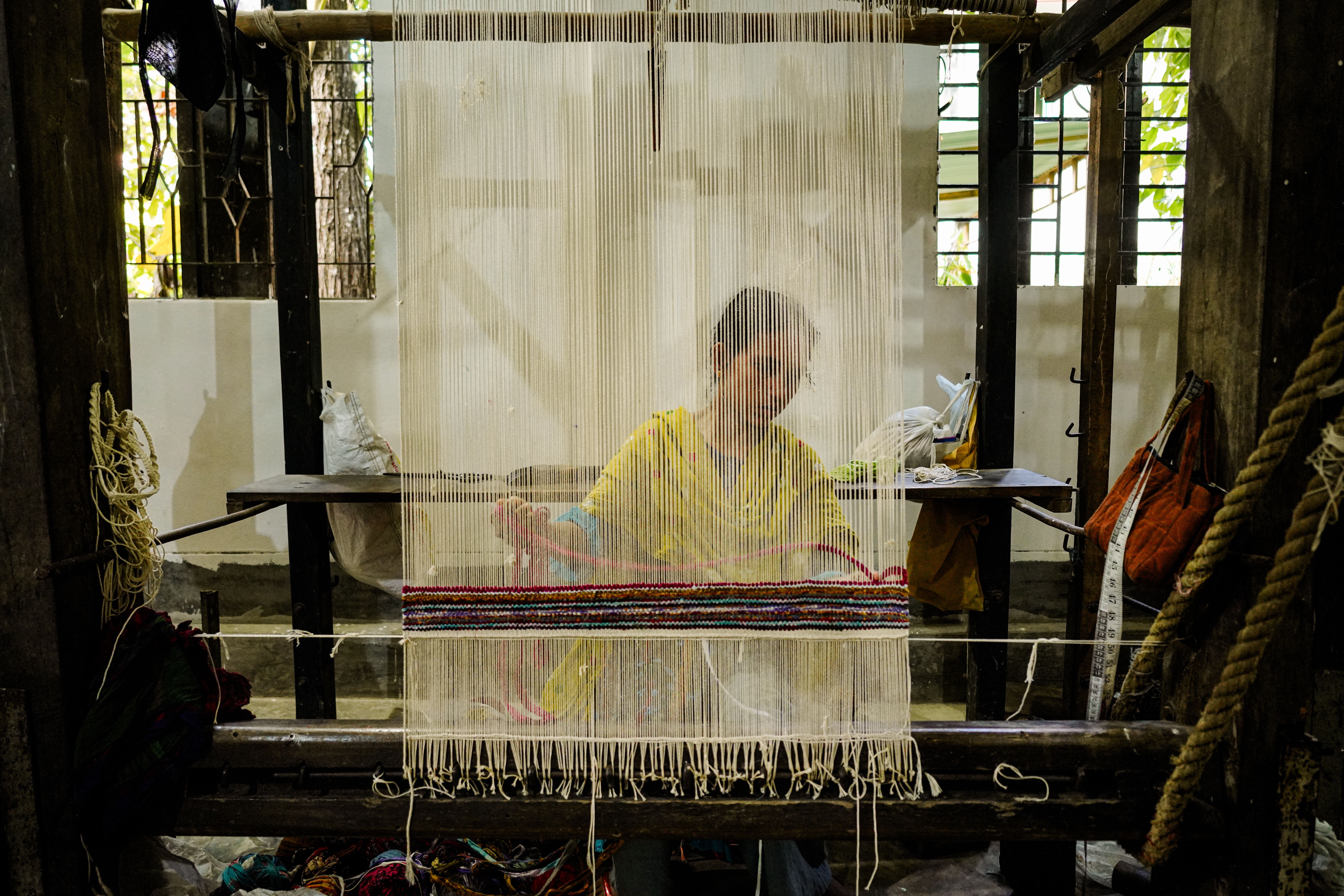 A woman weaving a colorful textile on a traditional loom in an indoor artisan workshop.