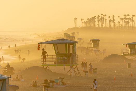 A golden sunset at Huntington Beach featuring lifeguard towers and silhouettes of people enjoying the tranquil evening.