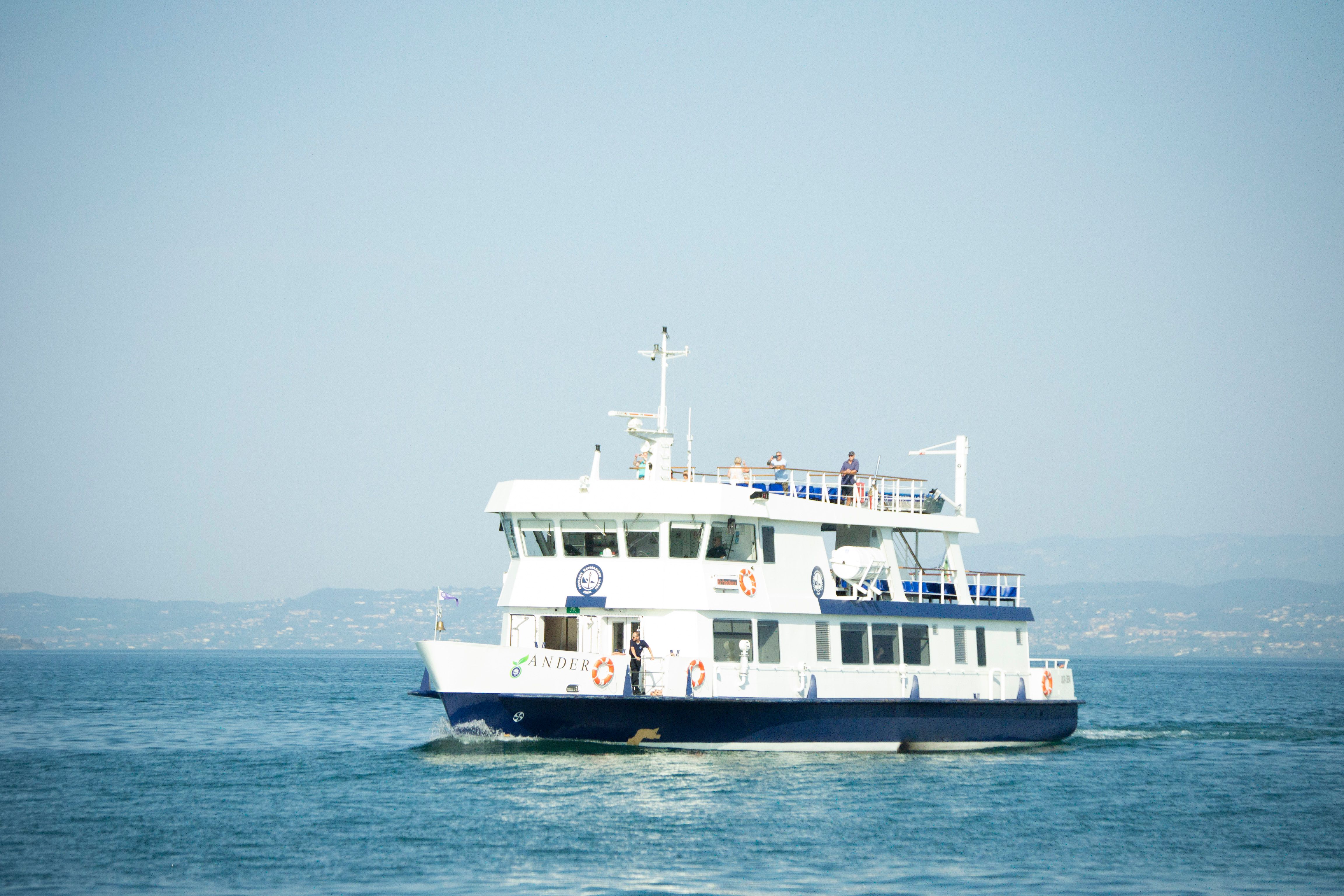 A passenger ferry cruises peacefully across calm waters with distant hills in the background.