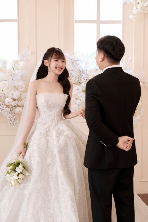 Free A joyful bride and groom holding hands, surrounded by white flowers indoors. Stock Photo
