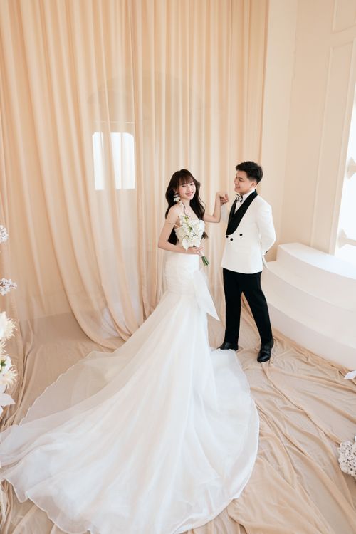Free A bride and groom pose gracefully indoors, showcasing wedding attire in a soft light setting. Stock Photo