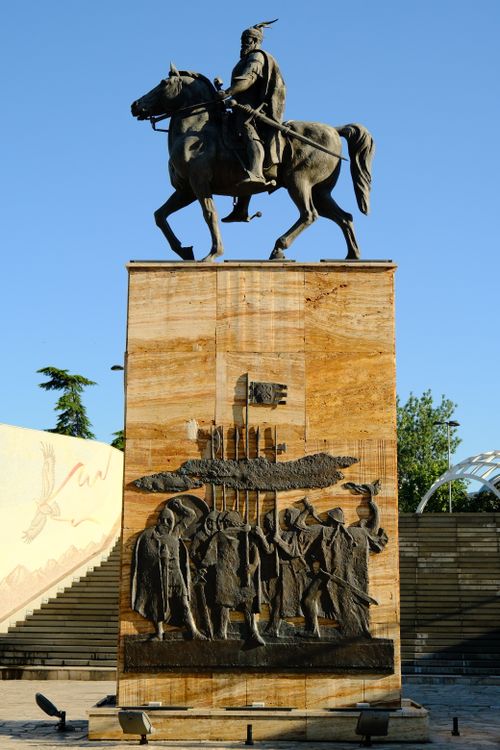 Free Equestrian statue on a pedestal with relief carvings, set against a clear blue sky. Stock Photo