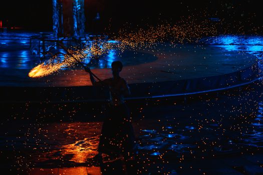 Performer silhouette swirling golden sparks on dark blue night stage