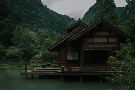 Traditional wooden house over calm water surrounded by lush green mountains