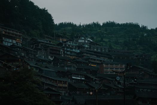 Traditional wooden village built on mountain slope wrapped in dim twilight soft light