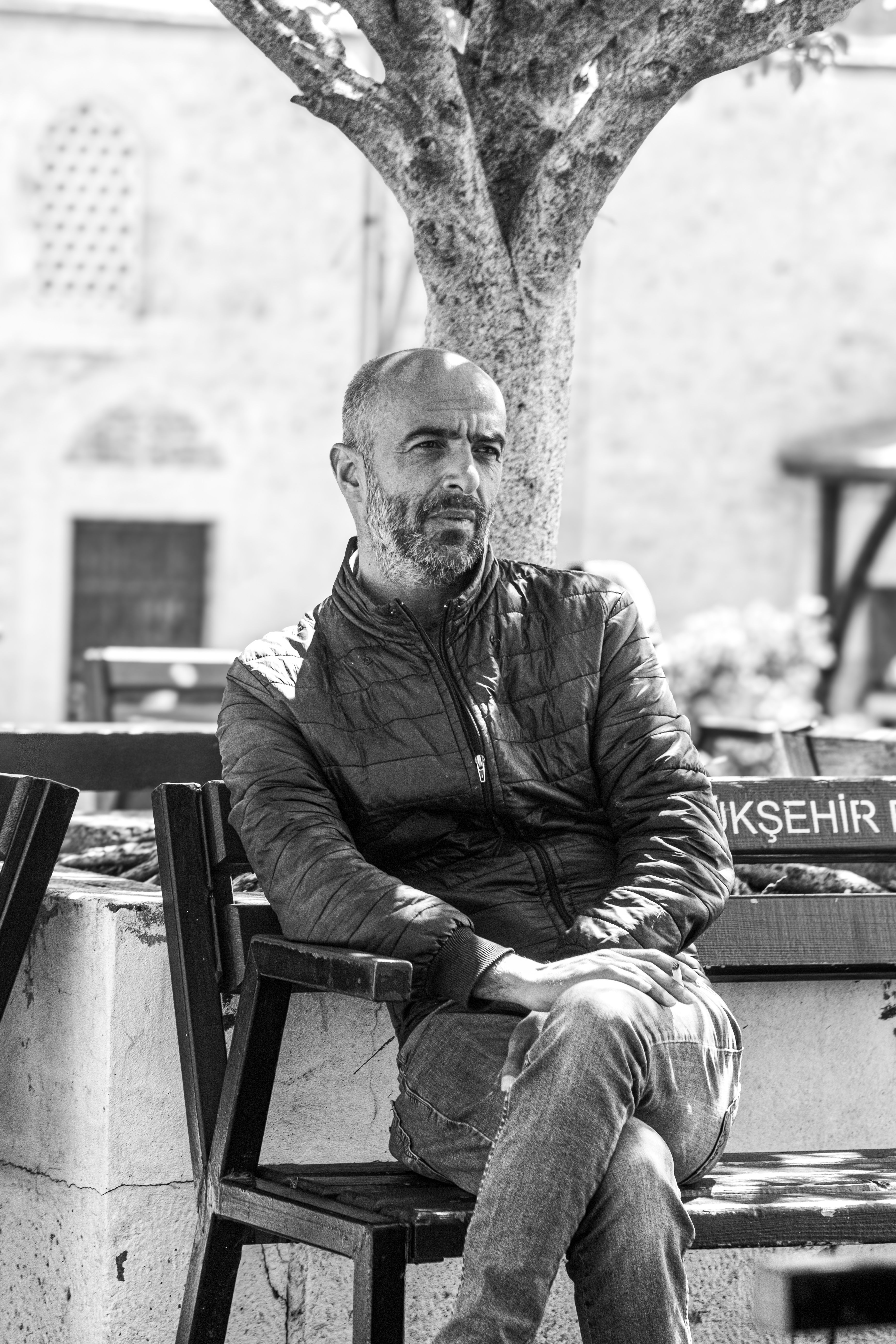 Black and white photo of a man sitting on a bench in an urban setting, exuding a reflective mood.