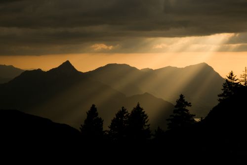 Free A breathtaking view of sun rays piercing through clouds over a mountain range at sunset. Stock Photo