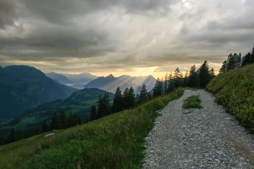 Free A breathtaking mountain path with sunset rays piercing through dramatic clouds over lush valleys. Stock Photo