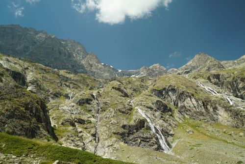 Free Breathtaking view of a rocky alpine mountain landscape with cascading waterfalls under a clear blue sky. Stock Photo